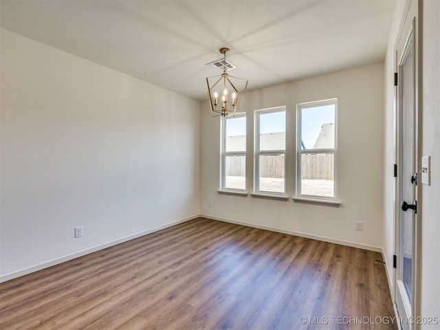 unfurnished room with visible vents, baseboards, an inviting chandelier, and wood finished floors