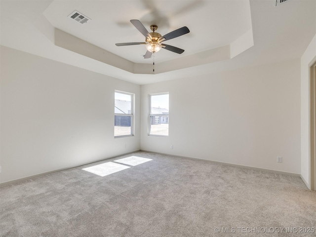 carpeted empty room with a tray ceiling, baseboards, visible vents, and ceiling fan