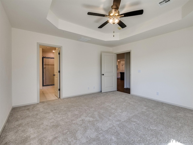 unfurnished bedroom featuring visible vents, baseboards, a tray ceiling, and carpet floors