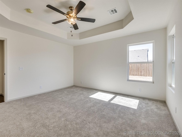 empty room with visible vents, baseboards, a tray ceiling, and carpet floors