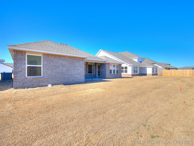 rear view of house with fence, central AC unit, brick siding, and a shingled roof