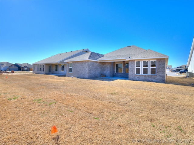 rear view of property with cooling unit, a lawn, and brick siding