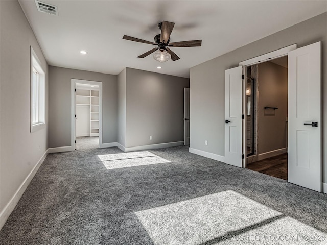 unfurnished bedroom with ceiling fan, a spacious closet, a closet, and dark colored carpet