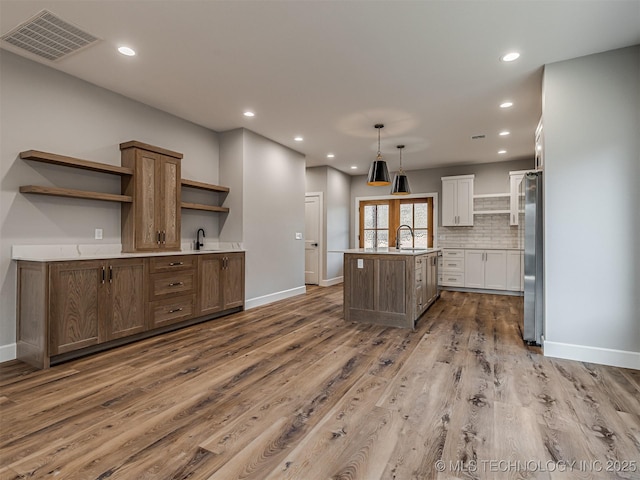 kitchen featuring sink, stainless steel refrigerator, pendant lighting, a kitchen island with sink, and white cabinets