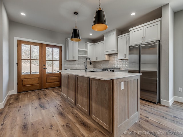 kitchen with stainless steel refrigerator, white cabinetry, light stone counters, a center island with sink, and decorative light fixtures