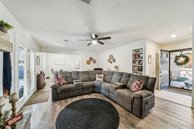 living room featuring ceiling fan, light hardwood / wood-style floors, and a textured ceiling