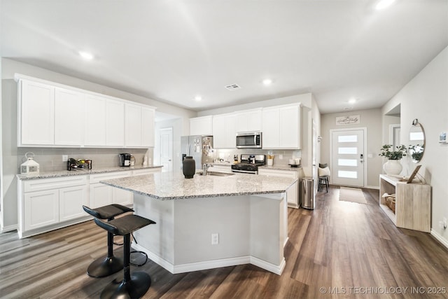 kitchen with white cabinets, a center island with sink, backsplash, and appliances with stainless steel finishes