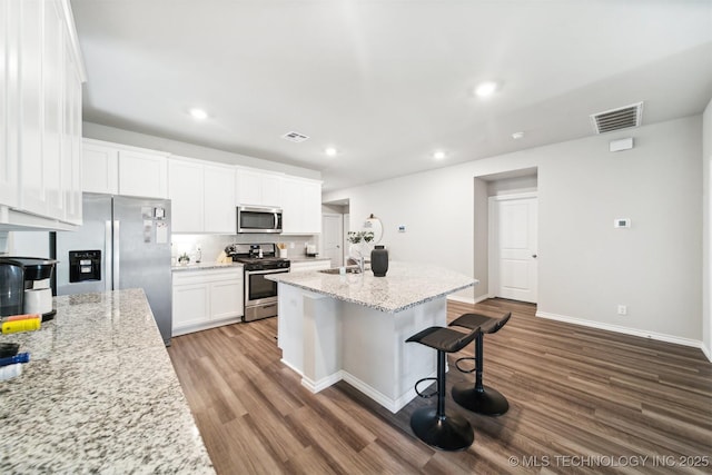 kitchen with hardwood / wood-style floors, white cabinets, a center island with sink, light stone counters, and stainless steel appliances