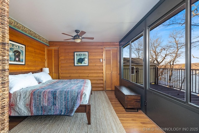 bedroom featuring light wood-type flooring, access to outside, rustic walls, and ceiling fan