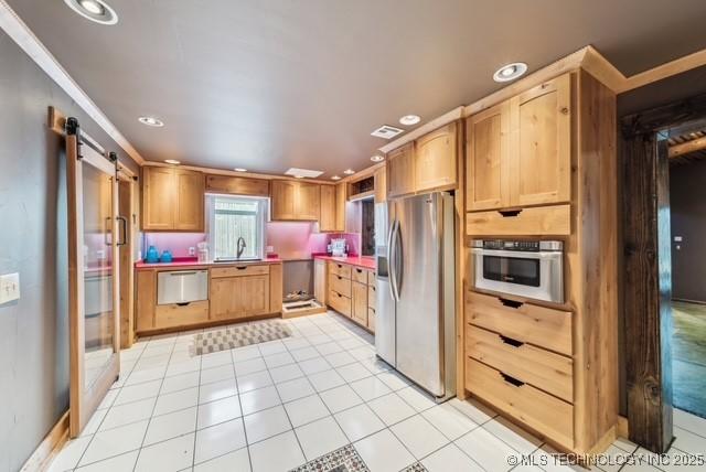 kitchen featuring sink, a barn door, appliances with stainless steel finishes, light tile patterned floors, and ornamental molding