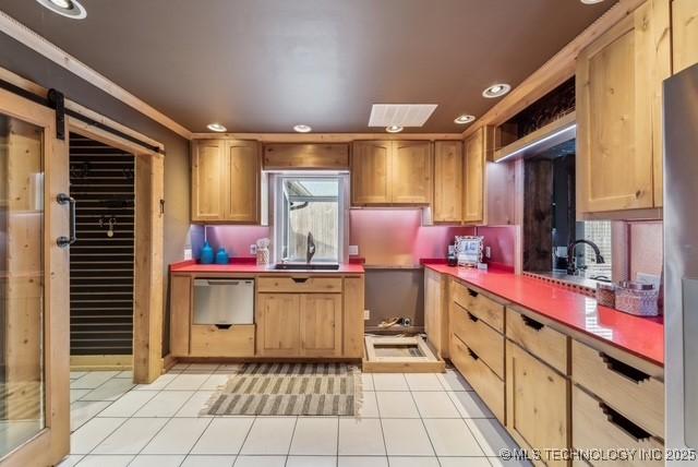 kitchen featuring stainless steel appliances, crown molding, sink, a barn door, and light tile patterned flooring