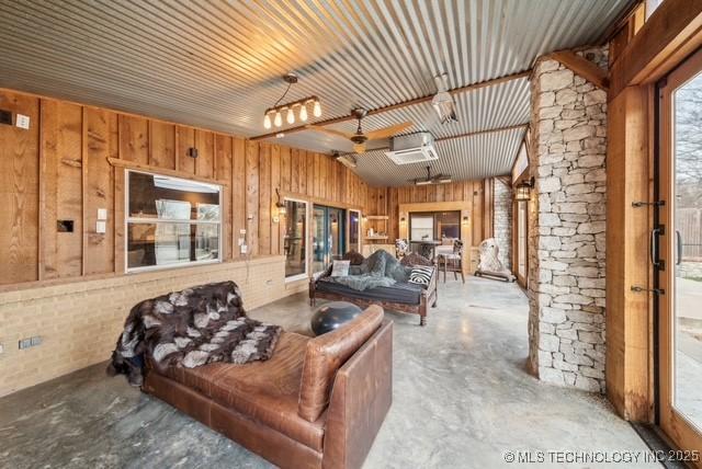 living room featuring ceiling fan, concrete flooring, and wooden walls