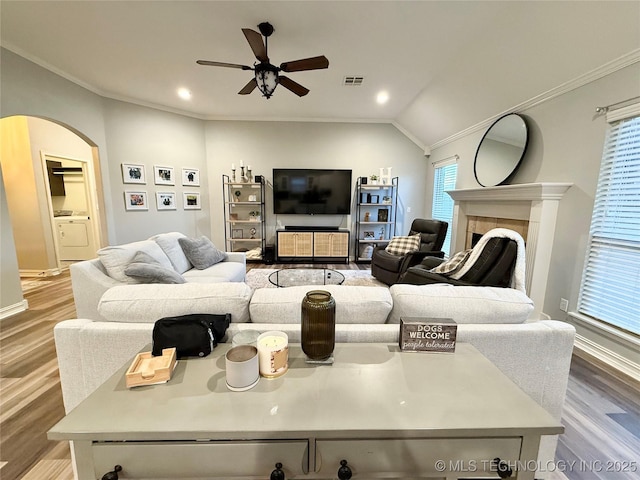 living room with arched walkways, wood finished floors, a ceiling fan, washer / dryer, and crown molding