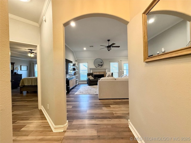 corridor featuring arched walkways, crown molding, baseboards, and wood finished floors