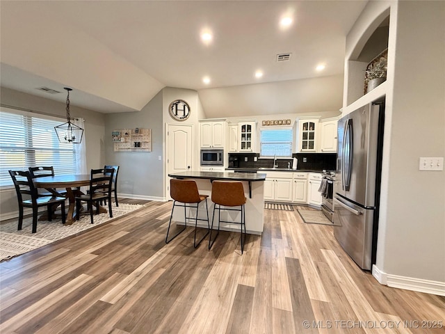 kitchen with visible vents, appliances with stainless steel finishes, a sink, a kitchen island, and a kitchen bar