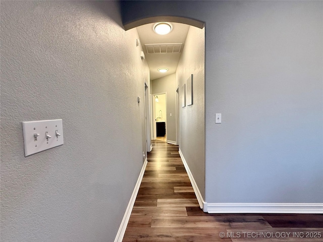 hallway featuring baseboards, visible vents, arched walkways, a textured wall, and wood finished floors