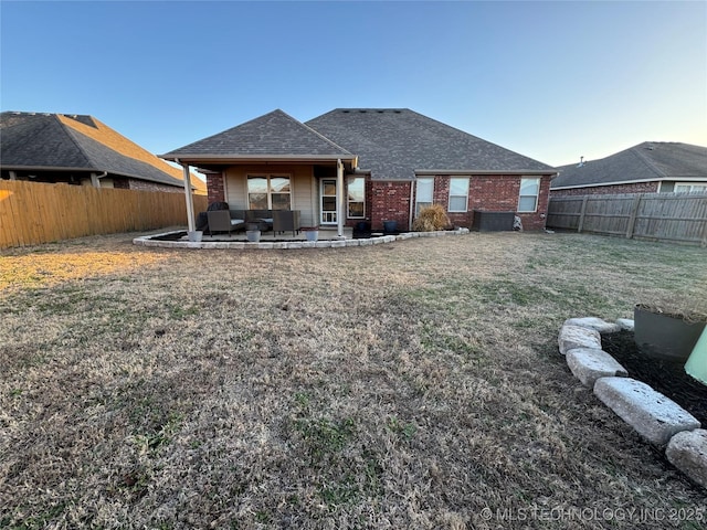 rear view of house featuring a shingled roof, a patio area, a fenced backyard, and brick siding