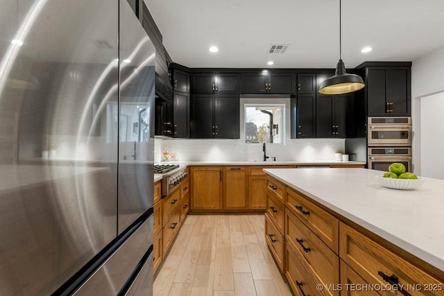 kitchen featuring pendant lighting, sink, light hardwood / wood-style flooring, tasteful backsplash, and stainless steel appliances