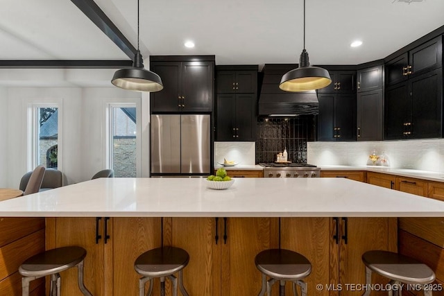 kitchen featuring backsplash, wall chimney range hood, a center island, stainless steel refrigerator, and hanging light fixtures