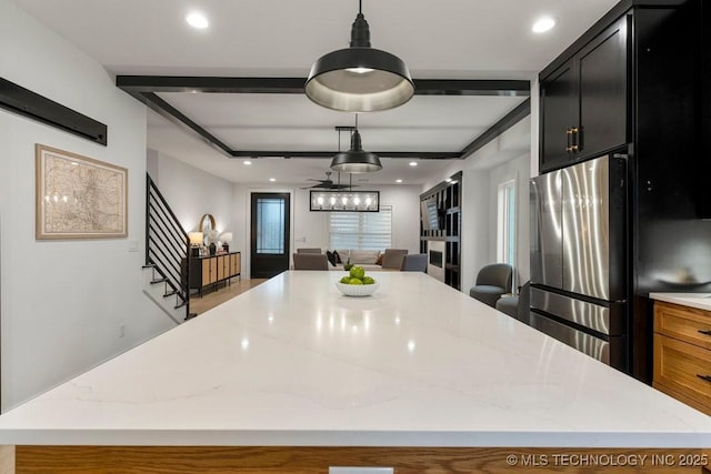 kitchen with pendant lighting, a center island, ceiling fan, stainless steel fridge, and light stone counters