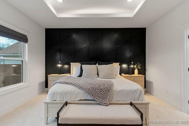 bedroom with a tray ceiling, light carpet, and baseboards