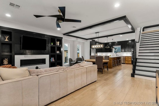 living room with ceiling fan with notable chandelier, light hardwood / wood-style floors, and sink