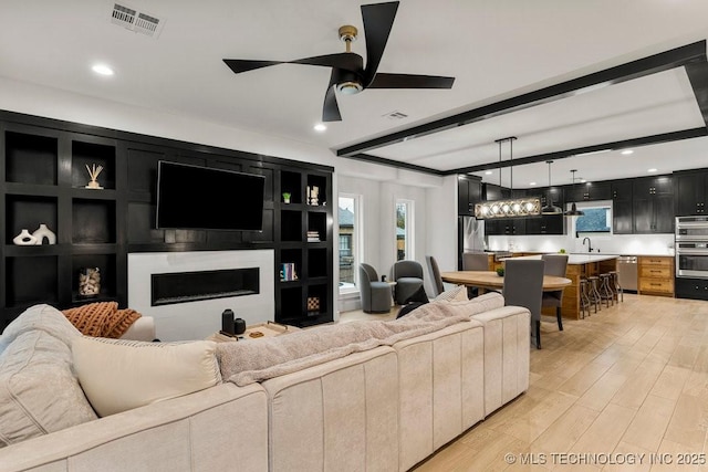 living area featuring ceiling fan, a fireplace, light wood-type flooring, visible vents, and beam ceiling