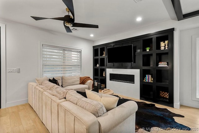 living room with built in shelves, ceiling fan, beamed ceiling, and light wood-type flooring