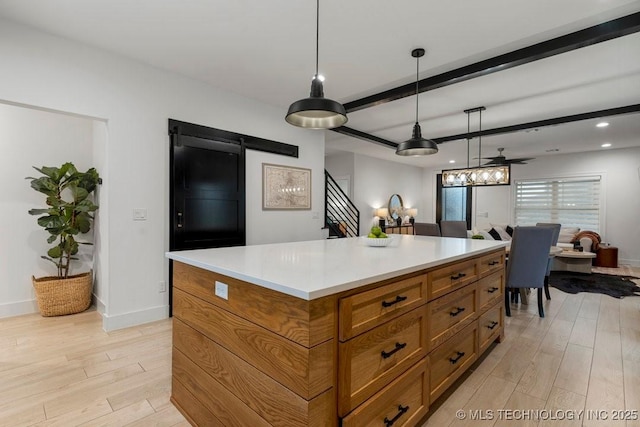 kitchen featuring ceiling fan, a barn door, decorative light fixtures, light hardwood / wood-style floors, and a kitchen island