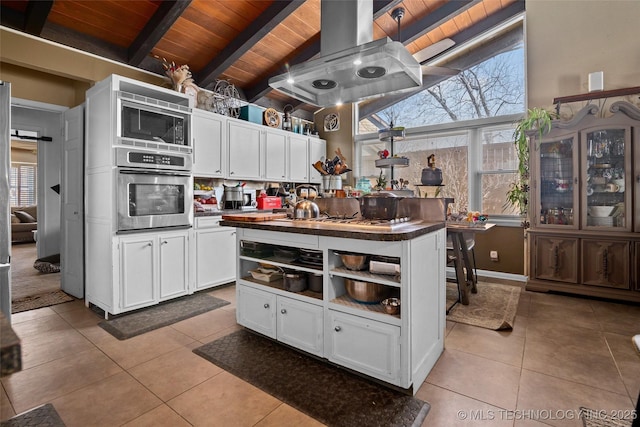 kitchen featuring stainless steel oven, island range hood, black microwave, beamed ceiling, and white cabinets