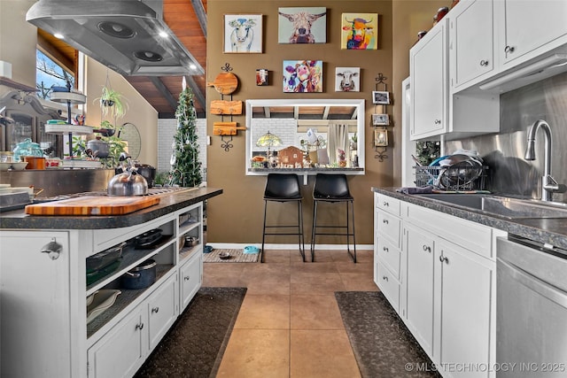 kitchen with tile patterned floors, wall chimney range hood, sink, stainless steel dishwasher, and white cabinetry