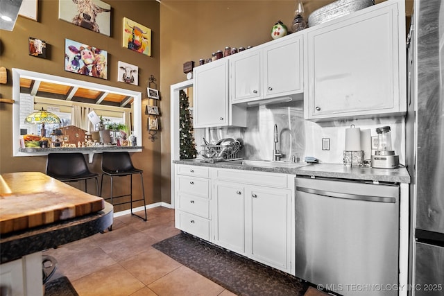 kitchen featuring dishwasher, backsplash, sink, light tile patterned floors, and white cabinetry