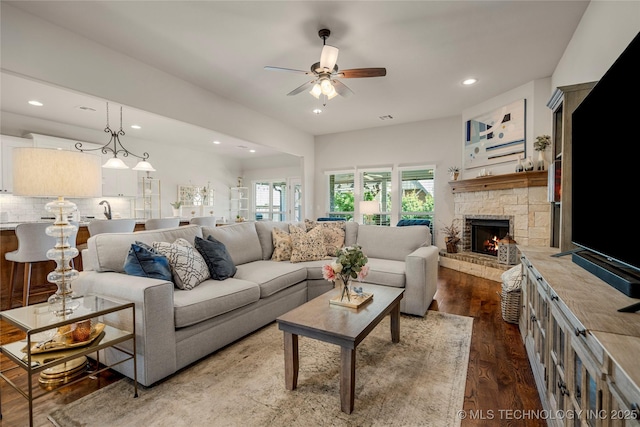 living room featuring dark hardwood / wood-style floors, ceiling fan, a stone fireplace, and sink