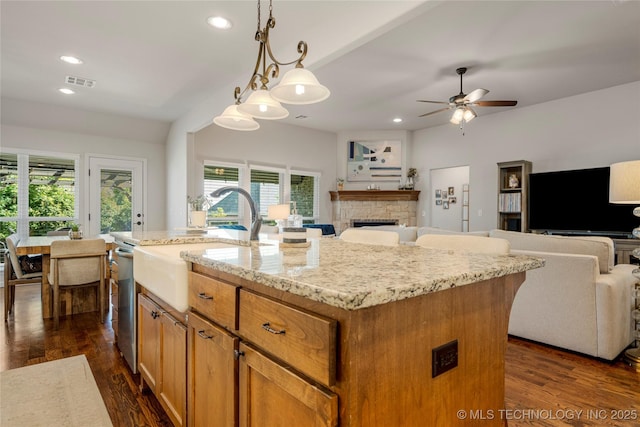 kitchen with ceiling fan, a healthy amount of sunlight, a fireplace, hanging light fixtures, and an island with sink