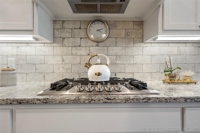 kitchen with light stone counters, white cabinetry, and backsplash