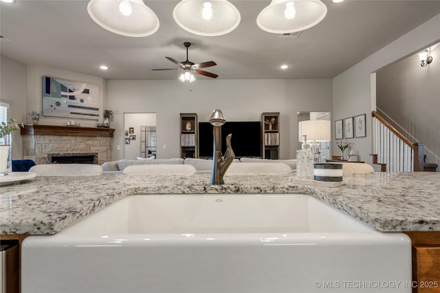 kitchen featuring light stone counters, ceiling fan, sink, decorative light fixtures, and a fireplace