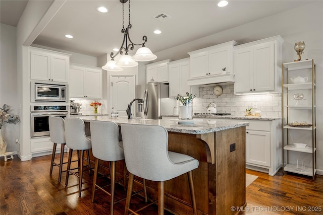 kitchen featuring white cabinets, an island with sink, stainless steel appliances, and dark hardwood / wood-style floors