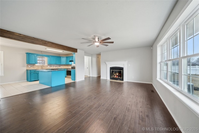 unfurnished living room with ceiling fan, beam ceiling, and light wood-type flooring