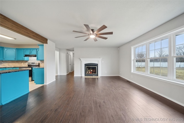 unfurnished living room with beam ceiling, ceiling fan, and dark hardwood / wood-style floors