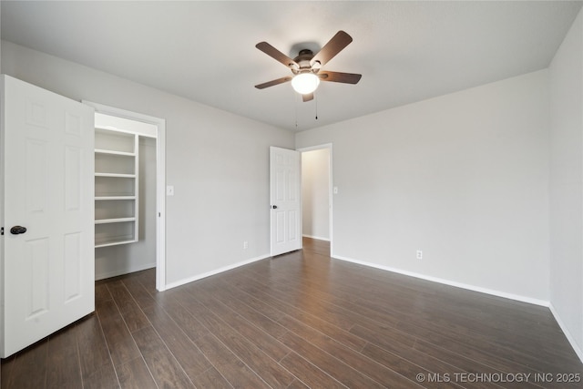 unfurnished bedroom with ceiling fan, a walk in closet, dark wood-type flooring, and a closet