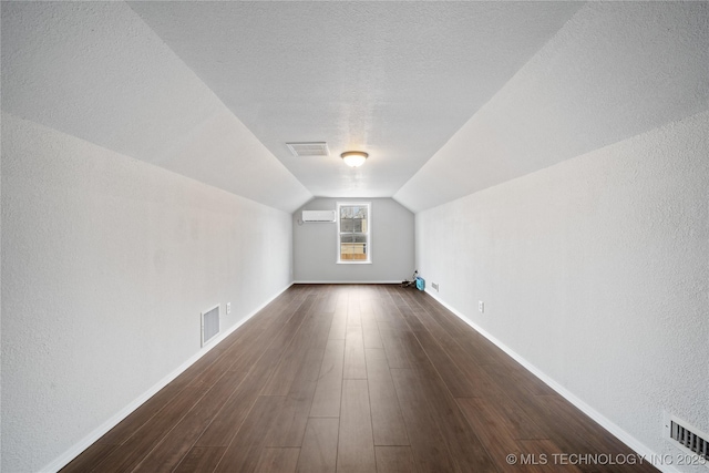 bonus room featuring a textured ceiling, an AC wall unit, vaulted ceiling, and dark wood-type flooring