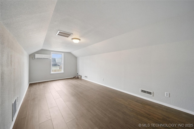 bonus room with a wall mounted air conditioner, wood-type flooring, a textured ceiling, and lofted ceiling