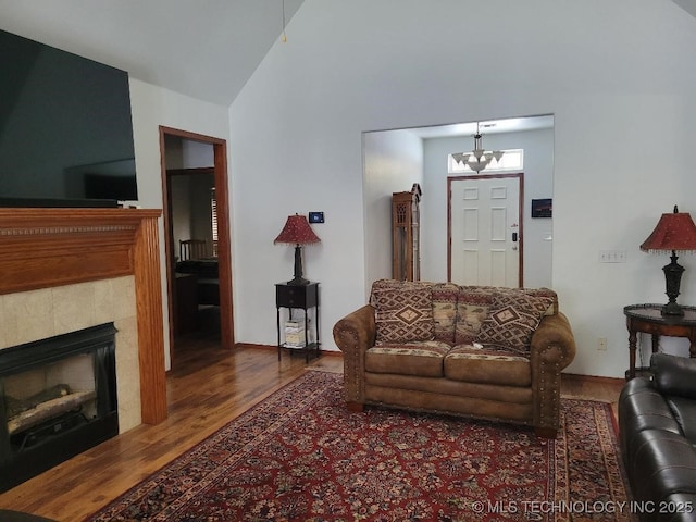 living room featuring a tile fireplace, wood-type flooring, vaulted ceiling, and a notable chandelier