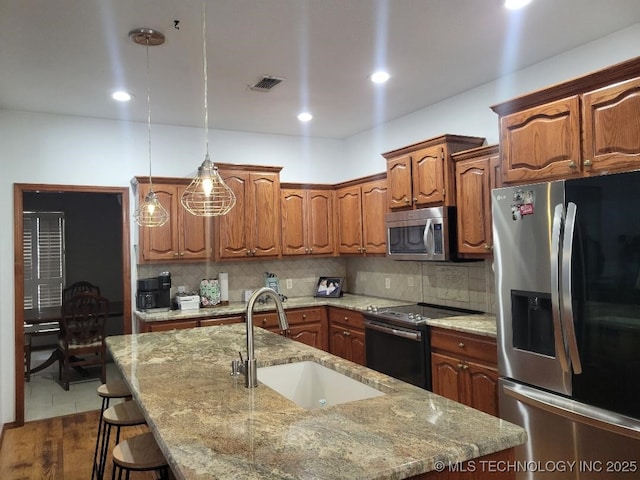 kitchen featuring pendant lighting, a kitchen island with sink, sink, appliances with stainless steel finishes, and tasteful backsplash