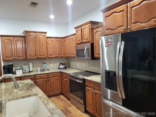 kitchen with light stone countertops, sink, appliances with stainless steel finishes, and tasteful backsplash