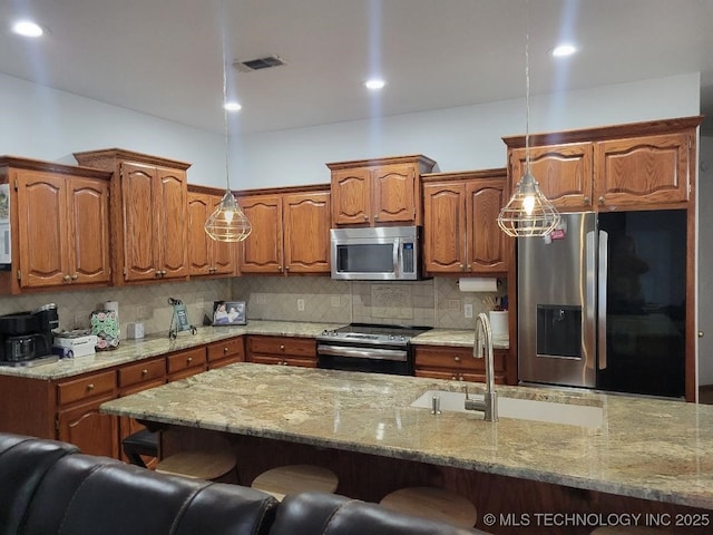 kitchen featuring pendant lighting, sink, decorative backsplash, appliances with stainless steel finishes, and a kitchen bar