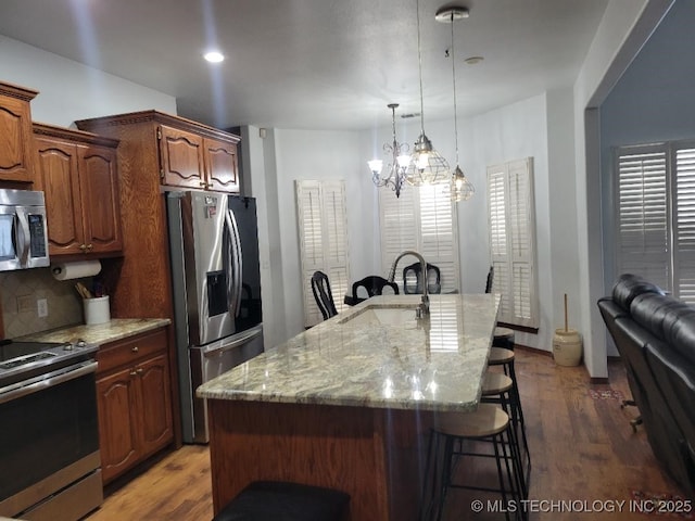 kitchen featuring a kitchen bar, appliances with stainless steel finishes, tasteful backsplash, a kitchen island with sink, and a notable chandelier