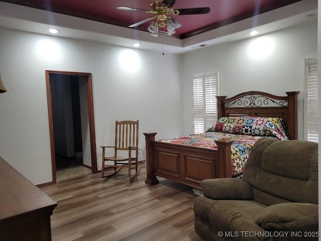 bedroom with light hardwood / wood-style floors, a raised ceiling, ceiling fan, and ornamental molding