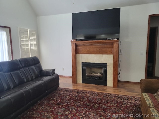 living room with hardwood / wood-style floors, lofted ceiling, and a tile fireplace