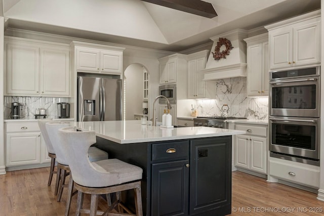 kitchen with white cabinets, lofted ceiling with beams, an island with sink, and appliances with stainless steel finishes